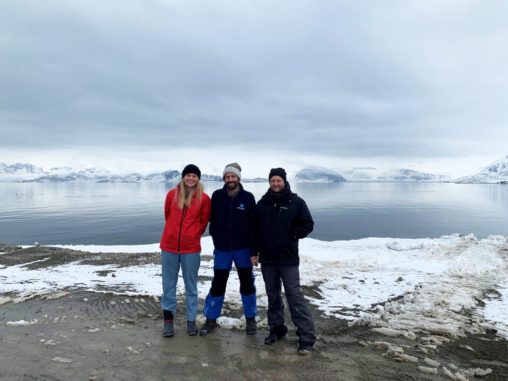 Three persons in front of sea and mountains